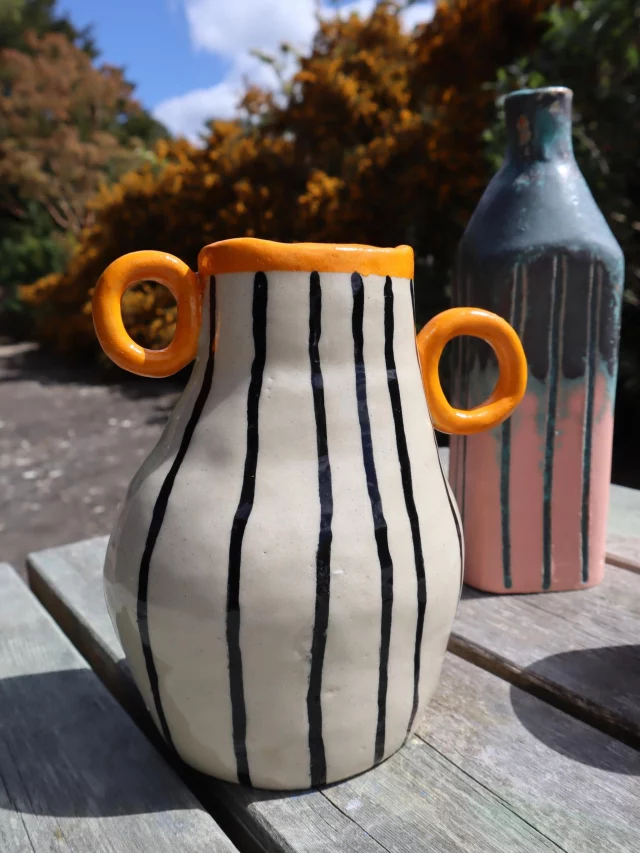 A playful approach to vase-making, using bold handles, hand-painted lines and colour to turn a functional form into something full of personality.